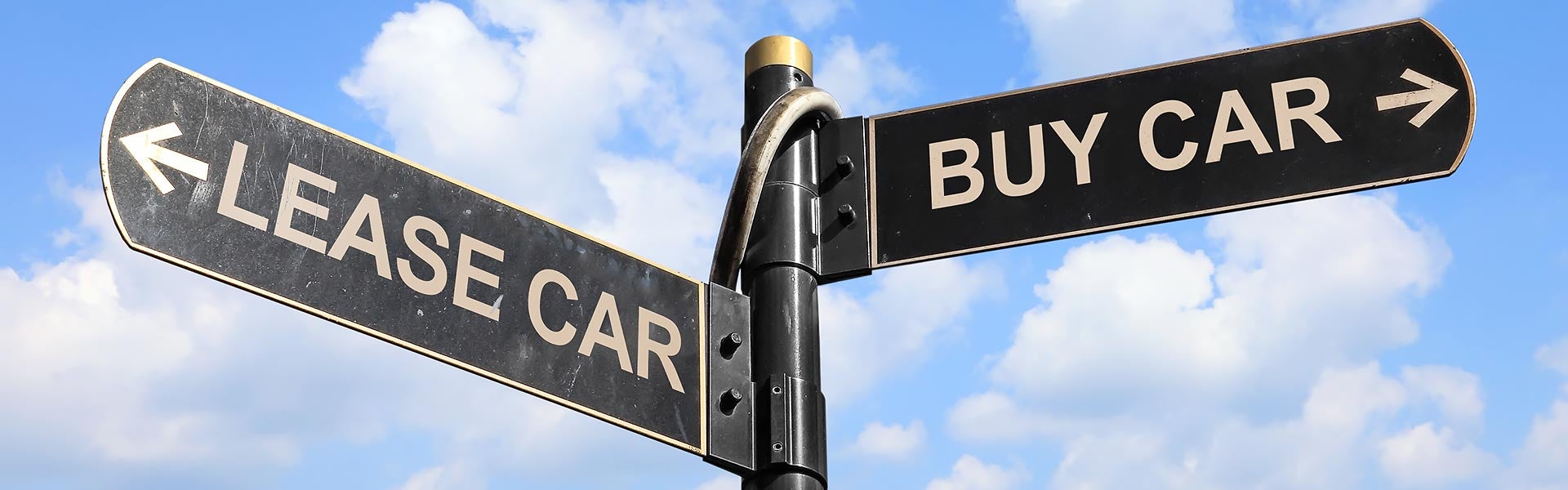 Directional street sign pointing left for "LEASE CAR" and right for "BUY CAR" against a blue sky.